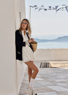 Woman in a stylish tennis dress with sunglasses and a woven bag by a coastal setting