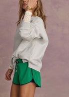Person wearing a gray oversized sweatshirt and green skirt against a purple background
